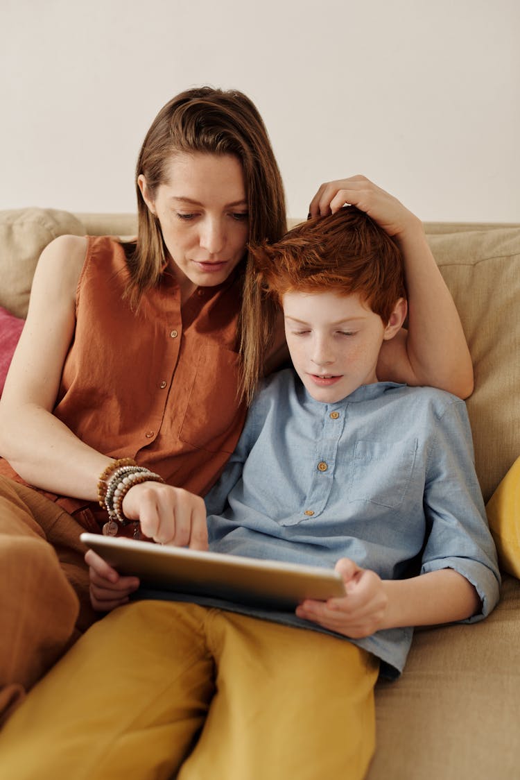 Photo Of Woman And Boy Sitting On Couch While Using Tablet Computer