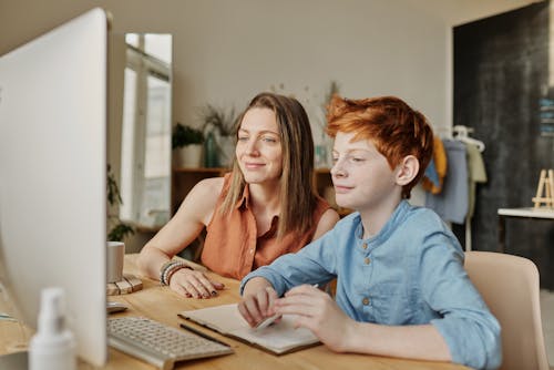 Photo of Woman and Boy Smiling While Watching Through Imac