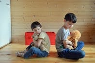 Sad little siblings hugging toys on floor