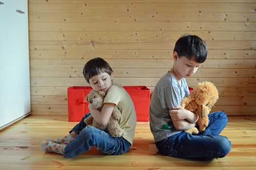 Sad little siblings hugging toys on floor