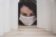 一名妇女戴着防护口罩，从卫生纸间窥视，凸显出大流行带来的焦虑