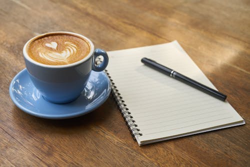 Free Coffee on Saucer Beside the Notebook Stock Photo