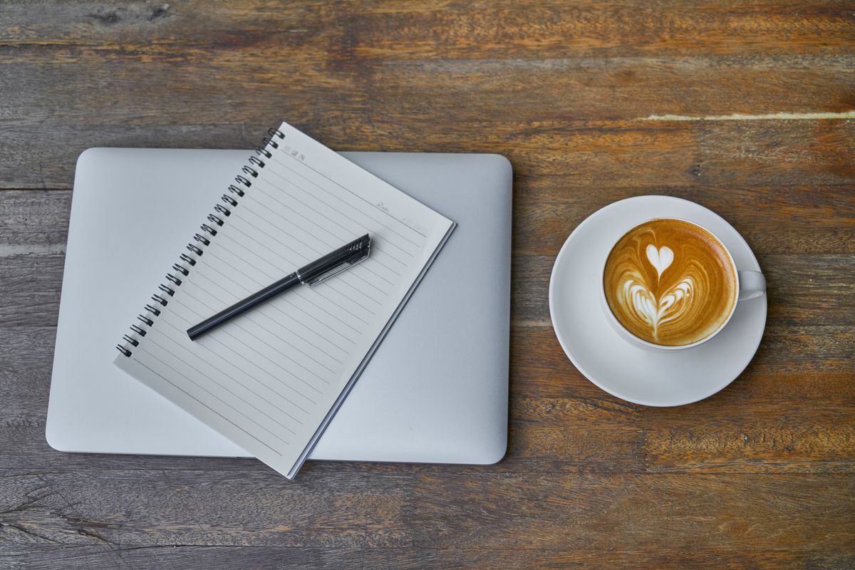 Flat lay of a coffee cup, notebook, pen and laptop on a rustic wooden table