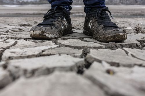 Free Close-up of muddy sneakers on cracked dry ground, symbolizing drought and resilience. Stock Photo