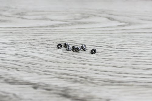 Close-Up Shot of Silver Screws on White Wooden Surface