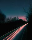 在德国星光灿烂的夜空下，一条树木繁茂的道路上留下了长时间曝光的汽车灯光痕迹