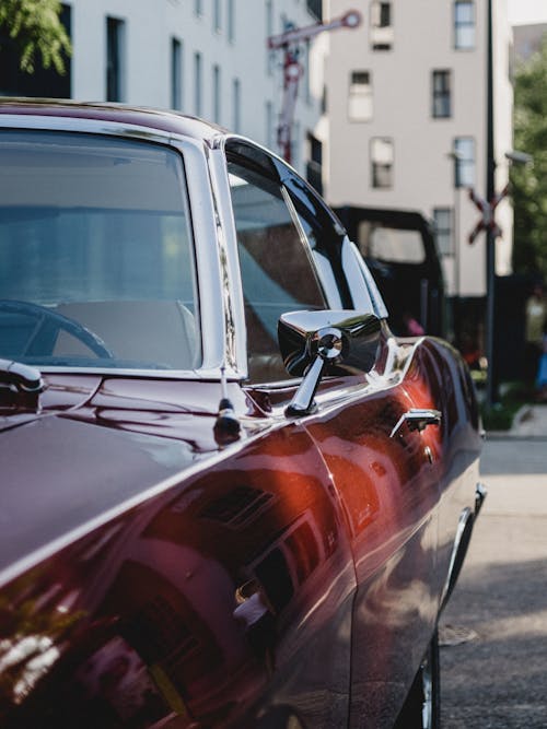 Vintage red shiny automobile parked on street against white facade of building at daytime