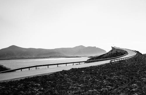 Black and white asphalt roadway going along calm sea and hills on shore