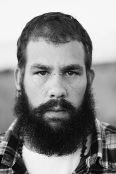 Close up black and white portrait of a serious bearded man with facial hair.