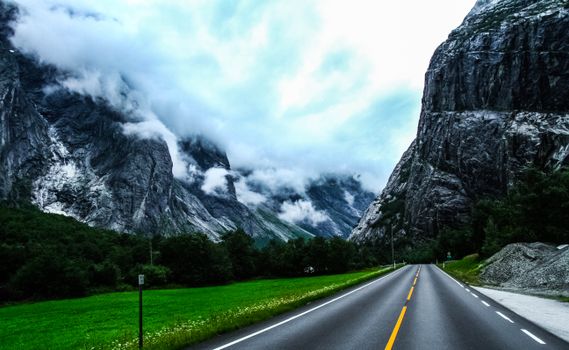 Picturesque scenery of highland covered with clouds and empty asphalt highway running among mountains and green plants