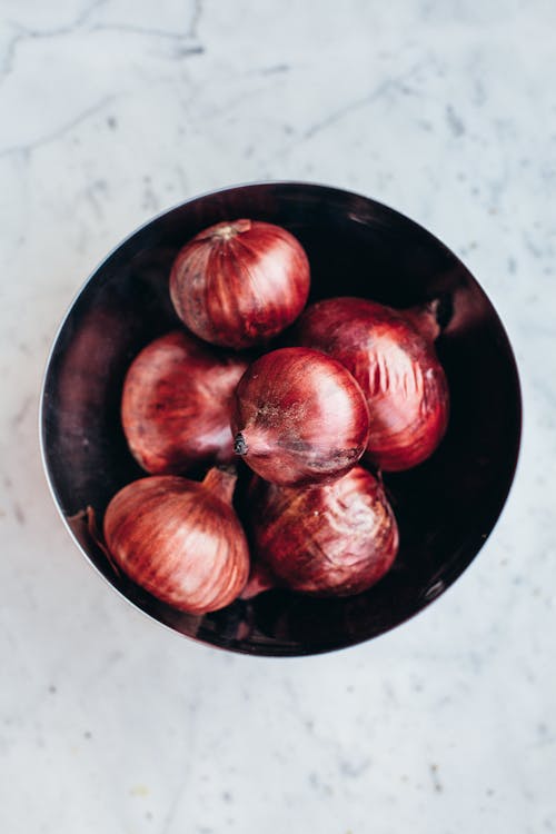 Free Top view black bowl with heap of fresh ripe unpeeled red onions placed on marble table Stock Photo
