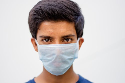 Free Close-up portrait of a teenager wearing a surgical face mask against a white background. Symbolizing health and safety. Stock Photo