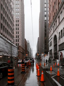 当代城市街道位于摩天大楼之间，雨天布满了现代车辆和路锥
