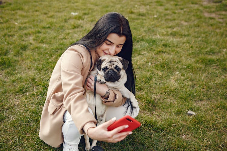 Woman In Brown Coat Holding Her Dog While Taking Selfie