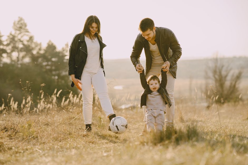 Una familia alegre jugando fútbol juntos en un campo iluminado por el sol, mostrando amor y unión.