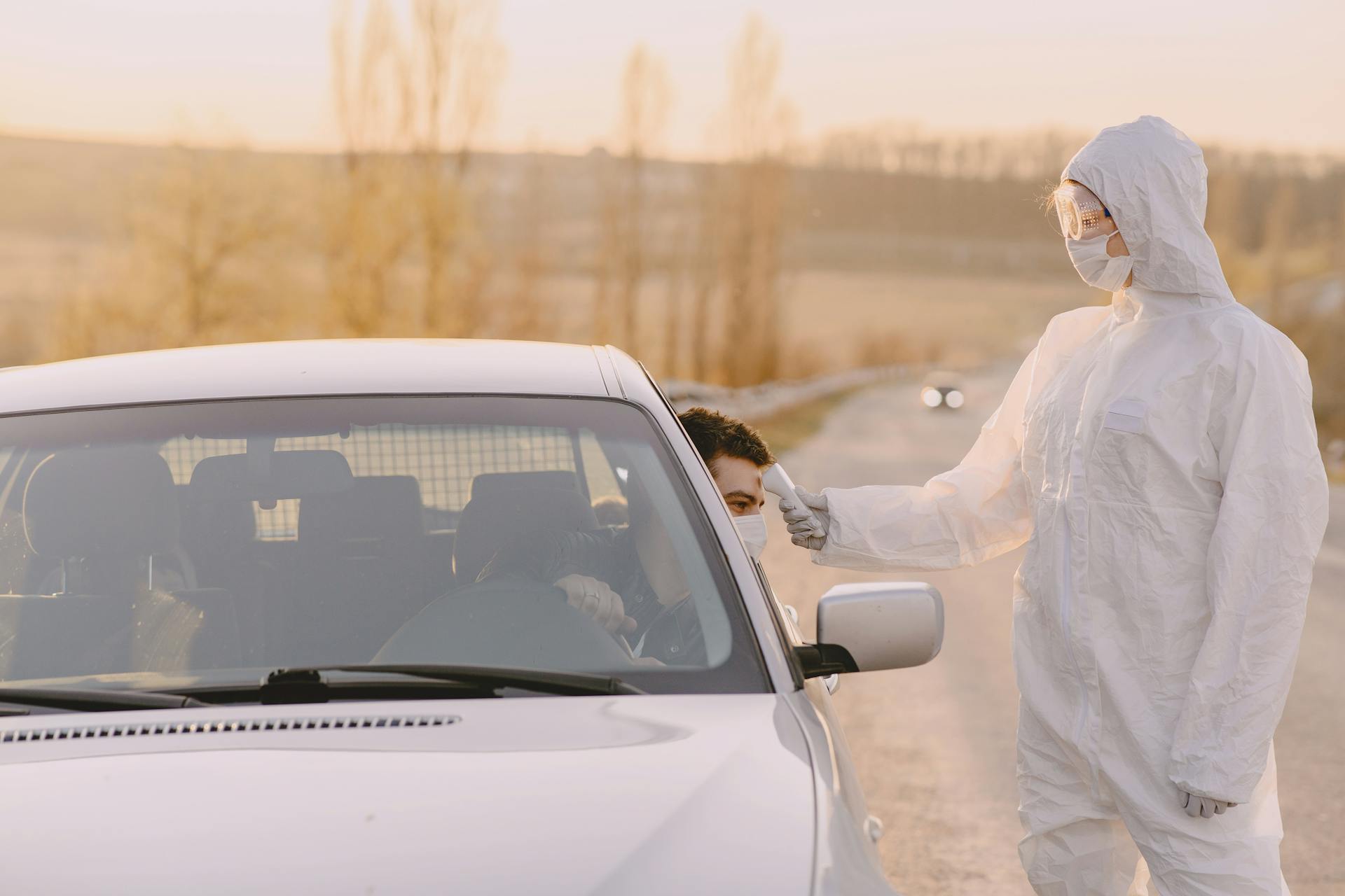 Photo of Person Wearing Personal Protective Equipment While Checking Temperature of a Man