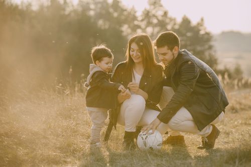 Free A cheerful family bonding outdoors with a soccer ball, enjoying a sunny day in the grass. Stock Photo