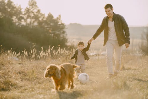 Photo of Man Holding His Child While Walking on Grass Field