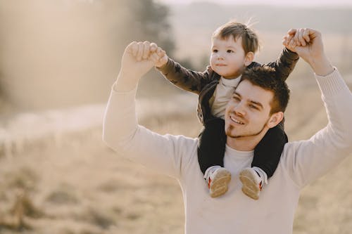 Photo of Man Carrying His Child While Raising Their Hands Up