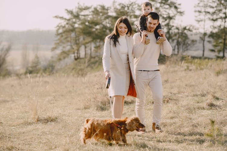 Photo Of Family Walking On Grass Field With Their Brown Dog