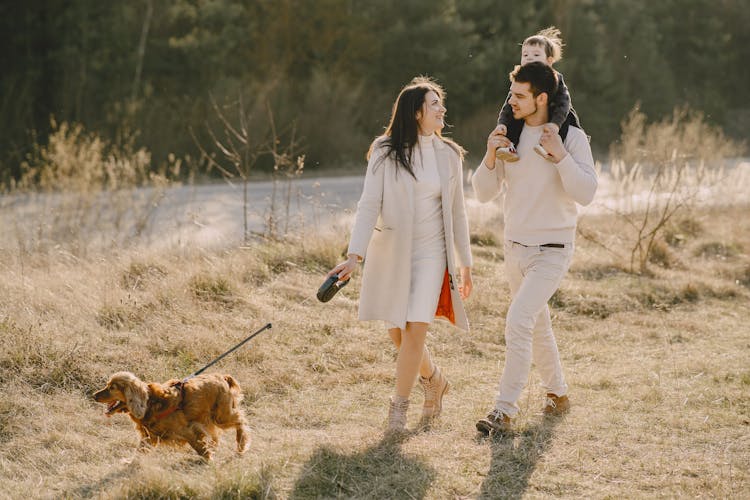 Photo Of Family Walking On Grass Field With Their Dog