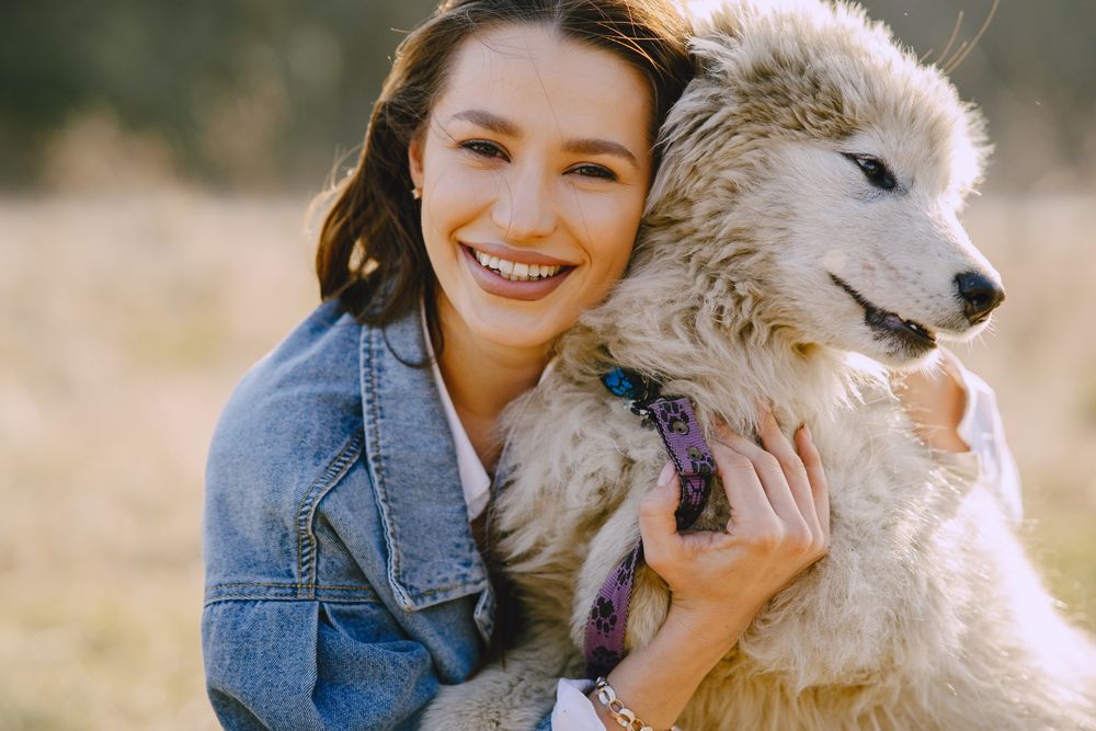 Smiling pet owner hugging a fluffy white dog
