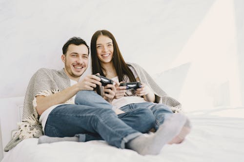 Happy couple playing game console while lying on bed