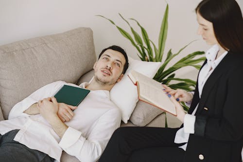 Thoughtful well dressed man with journal lying on sofa in office of modern female therapist and telling about problems