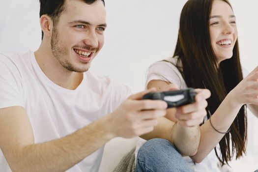 Crop happy man in white t shirt and jeans playing game pad while sitting with cheerful girlfriend in apartment on weekend