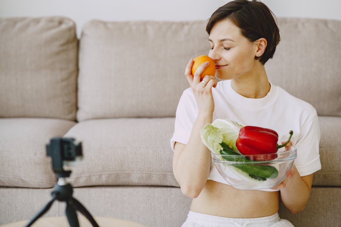 Photo of Woman Holding Orange Fruit and Bowl With Vegetables