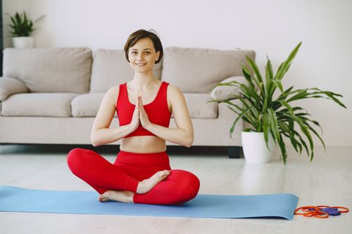 Free Happy female with short hair in sportswear sitting on yoga mat in living room near sofa and meditating while looking at camera Stock Photo