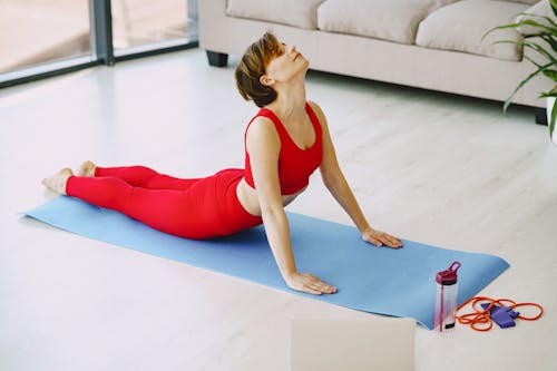 Focused female with short hair in activewear doing yoga asana on blue fitness mat in living room and looking up