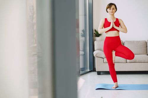 Free Full body of slim content female in activewear standing on mat in living room and balancing on one leg while looking at camera Stock Photo