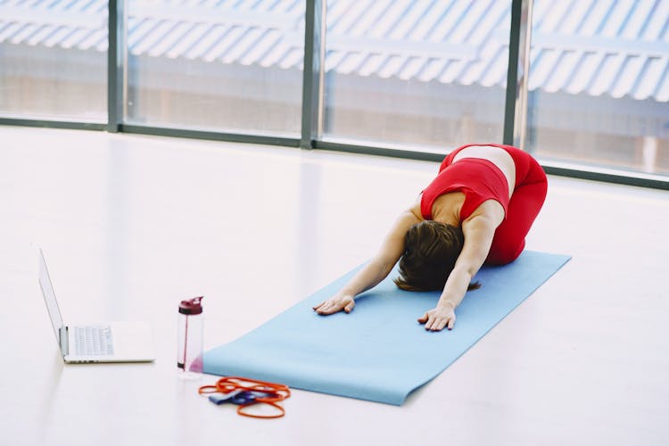 Young Woman Performing Yoga Exercise And Using Laptop At Home