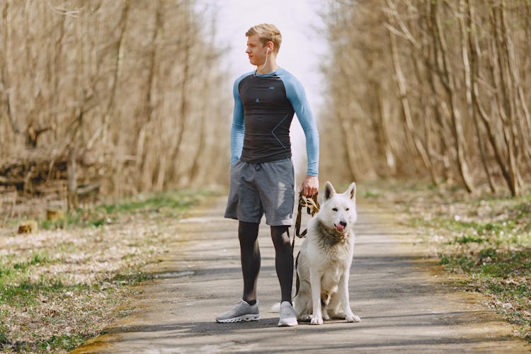 Confident Man Using Earbuds While Walking With Dog In Park In Spring