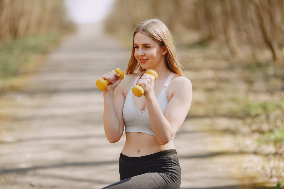 Fit woman lifting dumbbells on a sunny day, embracing a healthy outdoor workout.