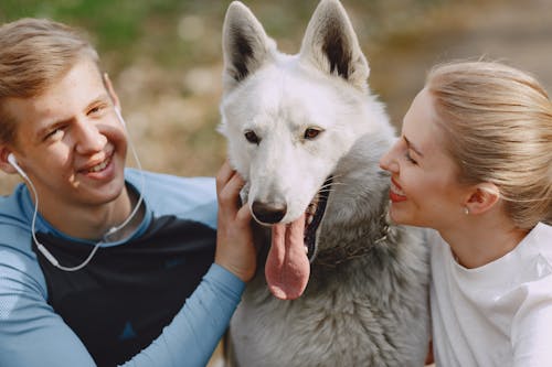 Photo of Man and Woman Smiling While Looking at White Dog