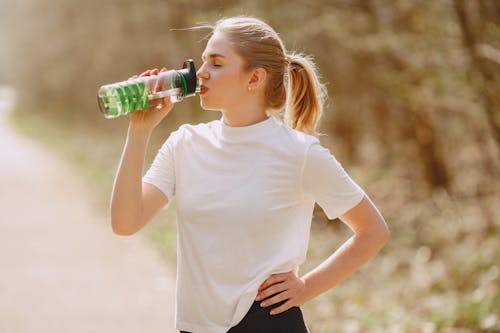 Free Woman in White Crew Neck T-shirt Drinking from Green Plastic Bottle Stock Photo