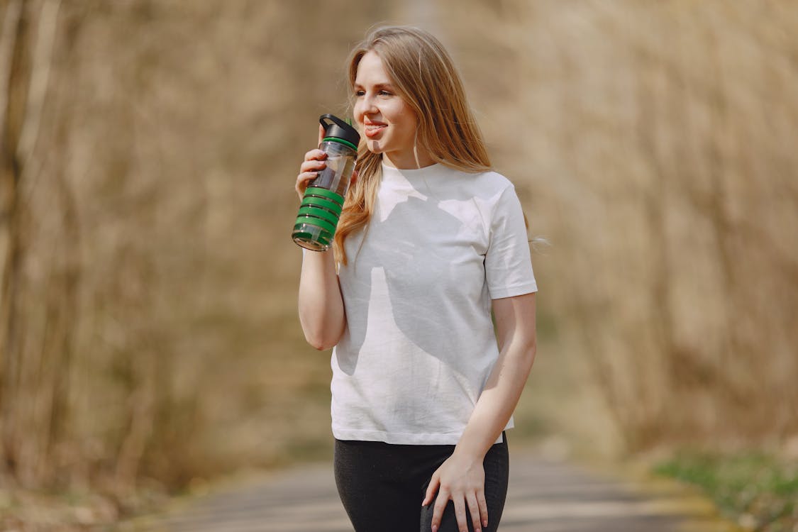 Lächelnde Frau trinkt Wasser während des Trainings im Park