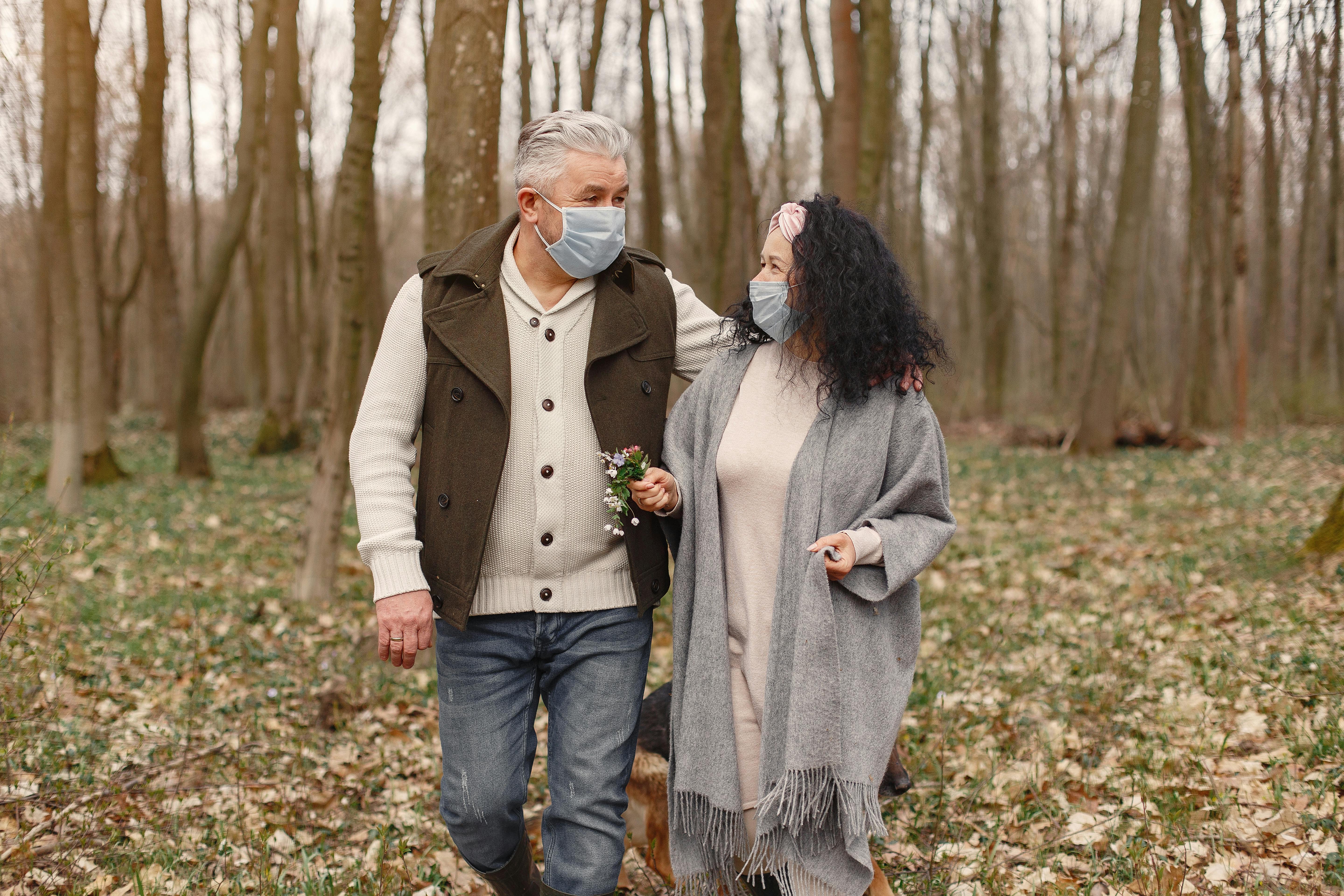 A senior couple enjoying a safe outdoor walk in the forest while wearing masks.