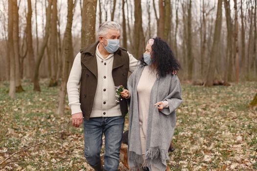 A senior couple enjoying a safe outdoor walk in the forest while wearing masks.