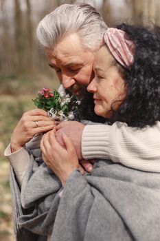 A serene moment of an elderly couple embracing each other with spring flowers in a forest setting. - Fotografer Sidoarjo