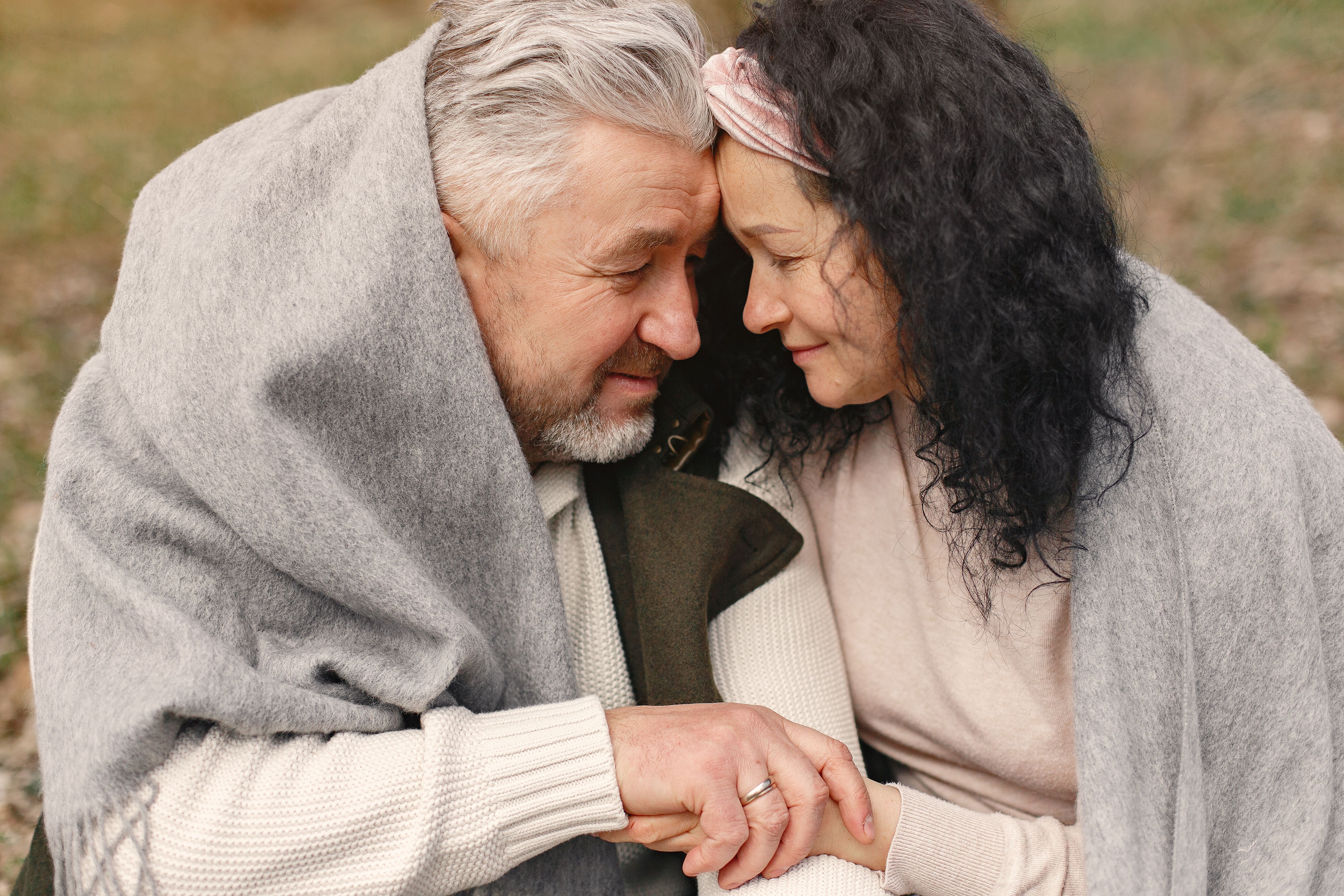 Close-up of a senior couple wrapped in a blanket sharing a tender moment outdoors.