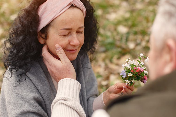 Happy Senior Woman With Delicate Flowers Strolling With Crop Husband In Nature