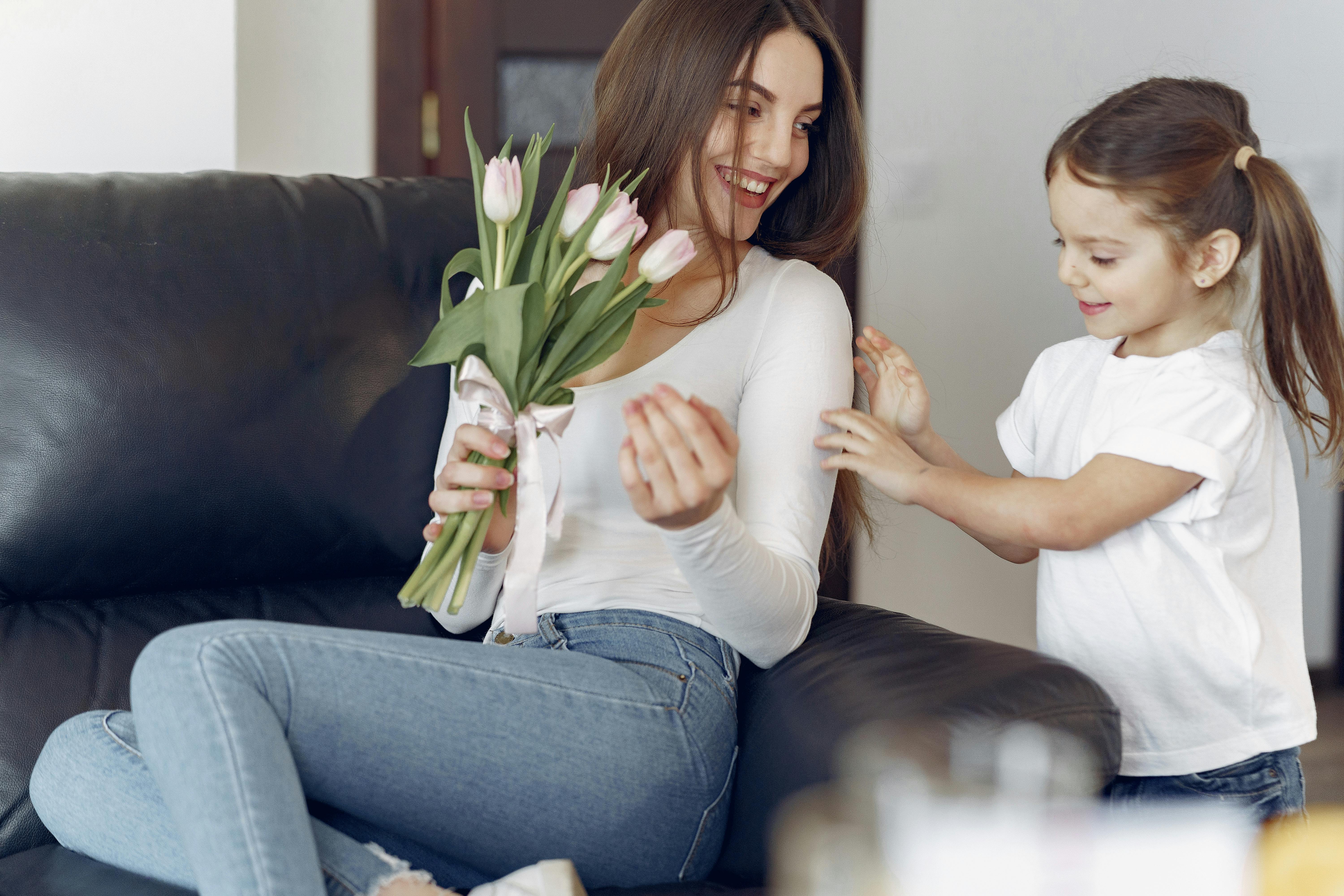 Happy mother and daughter giving flowers to mother at home