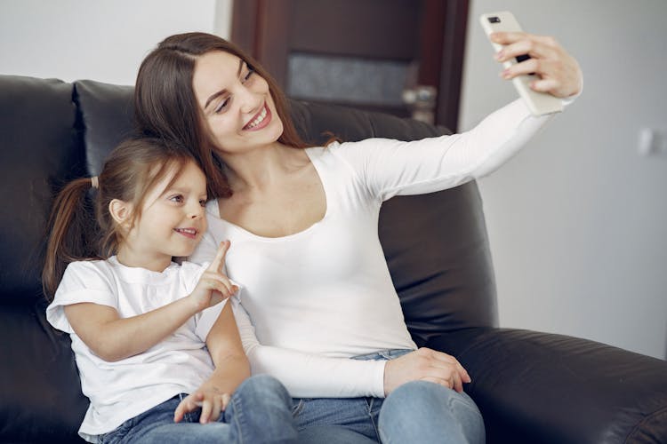 Smiling Mother And Daughter Taking Selfie On Smartphone At Home