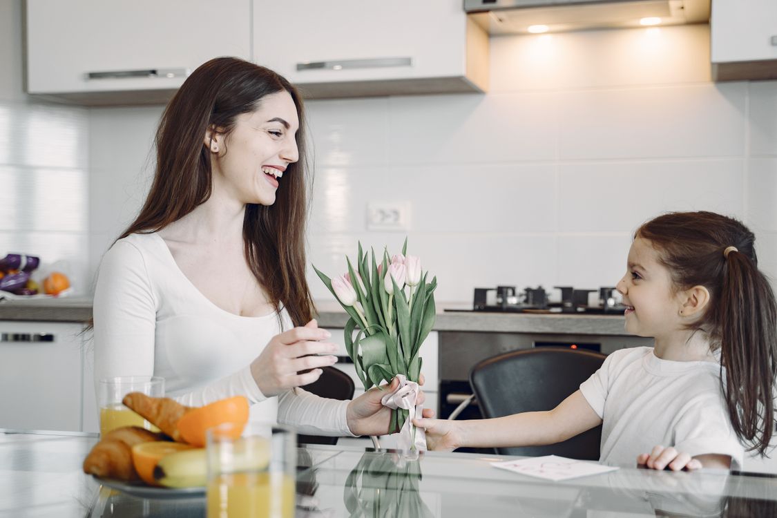 Good Morning Wishes 3 Happy girl presenting flowers to mother on kitchen