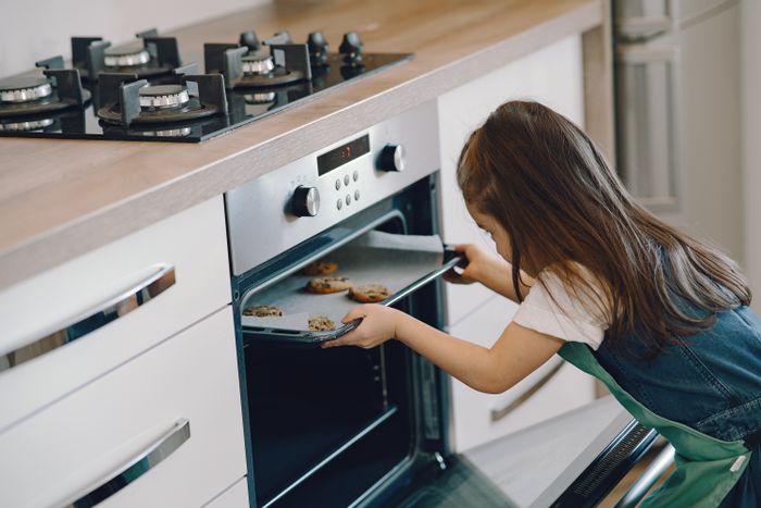Little baker sliding a tray of cookies into the oven