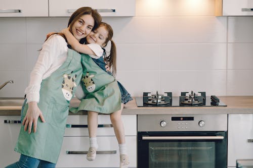 Photo of Girl Hugging Her Mom While Sitting on Kitchen Counter