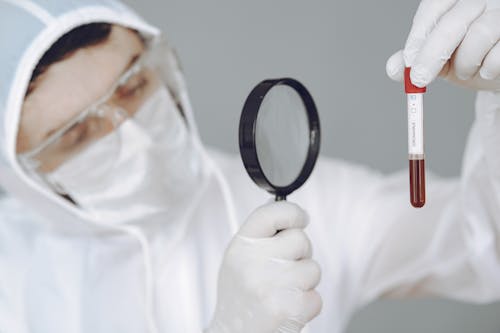 Person Holding Magnifying Glass and Test Tube